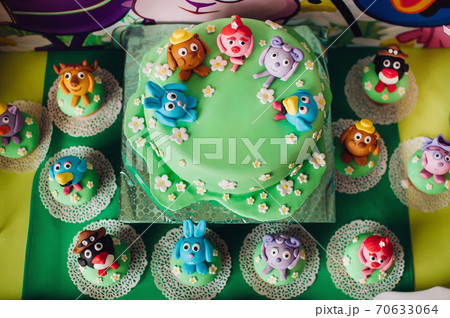 festive children's table with a beautiful cake decorated with green and multi-colored biscuits. candy. Children's birthday.Cake for children's birthday in cartoon style 70633064