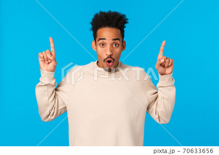 Have you seen it. Attractive impressed african-american guy with moustache, afro haircut, saying wow, telling about event, product advertising, pointing fingers up over blue background 70633656