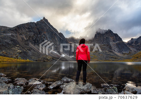 Woman Standing on a Rock at an Alpine Lake surrounded by Rugged Mountains 70637629