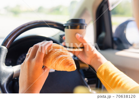 woman eating food fastfood and drink coffee while driving the car 70638120