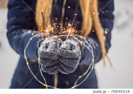 Sparklers in female hands on a background of snowfall. Christmas and New Year concept 70640319