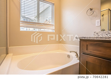 Bathroom interior with oval bathtub against white wall and window with blinds Bathroom interior with oval bathtub against white wall and window with blinds 70642281