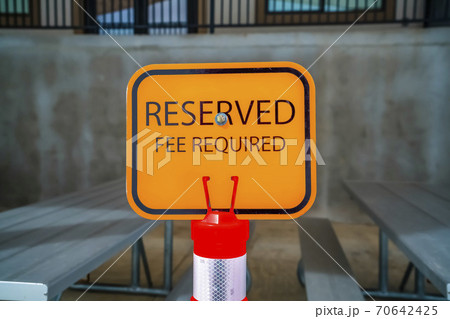 Close up of an orange Reserved sign with tables and benches in the background 70642425