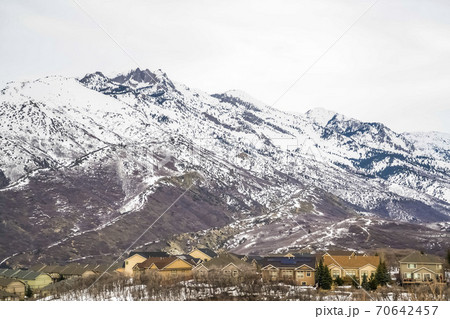 Residential area at the base of a towering snowy mountain against cloudy sky Residential area at the base of a towering snowy mountain against cloudy sky 70642457