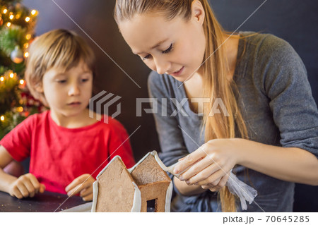 Young mother and kid making gingerbread house on Christmas eve Young mother and kid making gingerbread house on Christmas eve 70645285