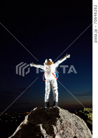 Spaceman standing on rocky hill under beautiful night sky. 70646262