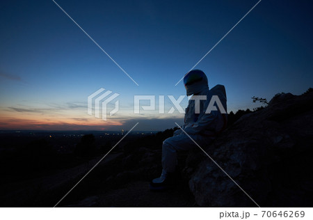 Astronaut sitting on rocky hill during sunset. Astronaut sitting on rocky hill during sunset. 70646269