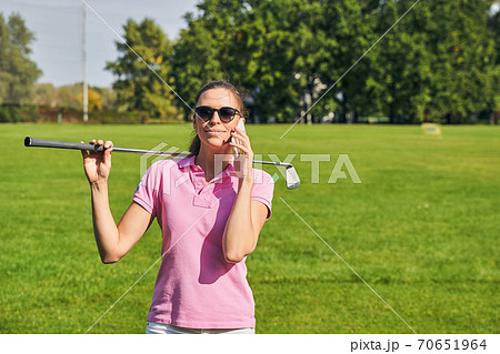 Smiling female with a golf club calling on her cellphone 70651964