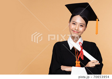 Happy Graduate asian woman in cap and gowm holding Certificated or diploma on Beige background,Graduation Concept 70653954