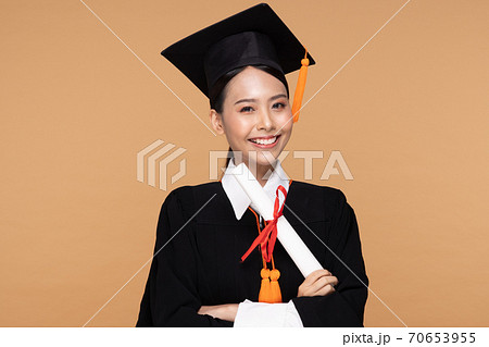 Happy Graduate asian woman in cap and gowm holding Certificated or diploma on Beige background,Graduation Concept 70653955