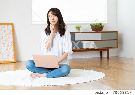 リビングであぐらをかいてノートパソコンを見る困った顔の若い女性 リビングであぐらをかいてノートパソコンを見る困った顔の若い女性 70655817