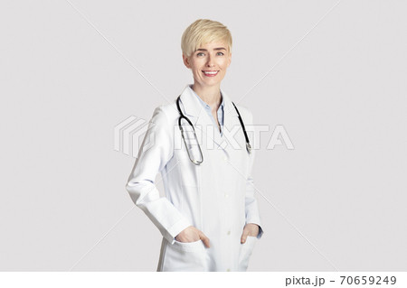 Attractive adult woman in white coat with stethoscope, puts hands in pockets Attractive adult woman in white coat with stethoscope, puts hands in pockets 70659249