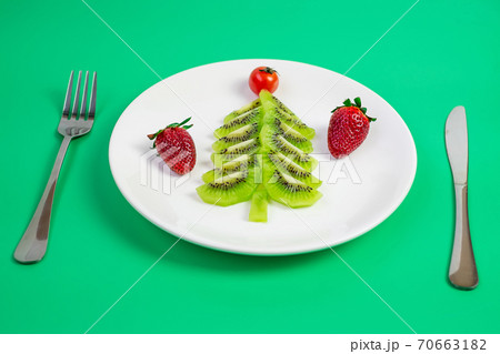 Christmas tree of organic vegetable and fruit; Kiwi, Strawberry and tomato with fork and knife on green background. Merry Xmas and happy New Year party, New You, Healthy food and vegetarian concept 70663182