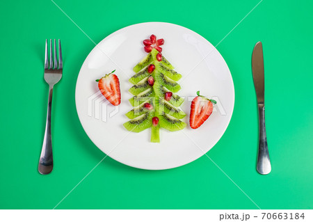Christmas tree of vegetable and fruit; Kiwi, Strawberry and Pomegranate seed with fork and knife on green background. Merry Xmas and happy New Year party, New You, Healthy food and vegetarian 70663184