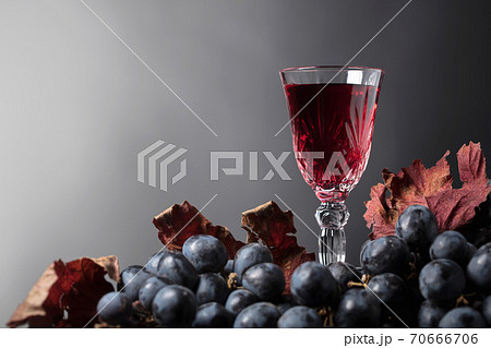 Crystal glass of red wine and grapes with dried vine leaves. Crystal glass of red wine and grapes with dried vine leaves. 70666706