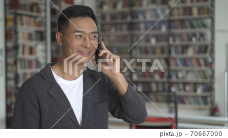 Young smiling asian man talking on the phone, teeth braces, in library 70667000
