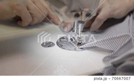 Sewing striped cloth on a white sewing machine close up, female hands 70667007