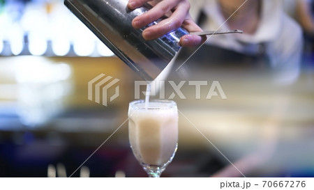 Bartender holding metal cup, pouring cocktail into a glass, lens flare 70667276
