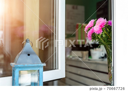 Open window with pink daisy flowers in vase of street city urban cafe with tee or coffee to go and warm sunrise sun reflection in glass. Welcome hospitality concept. Interior fresh plant decoration 70667726