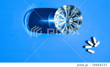Glass of water and white pills on blue background with hard light and shadows. Creative. White tablets and drink on blue background. Vitamins and prebiotics 70668335