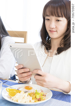 タブレットPCを見ながら食事する女性 70670907