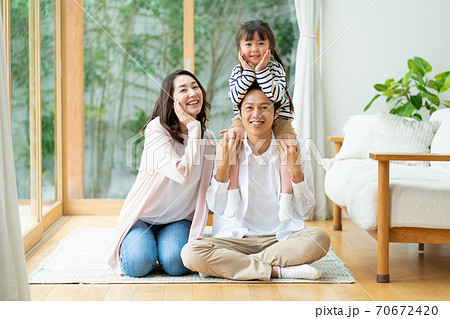 パパに肩車されてポーズをとる女の子とパパとママの3人家族のポートレートの写真素材