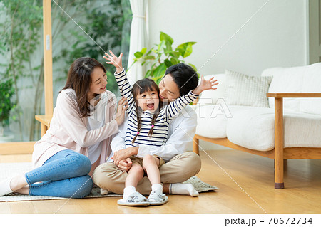 パパの膝に抱っこされる女の子とパパとママの笑顔の3人家族のポートレートの写真素材