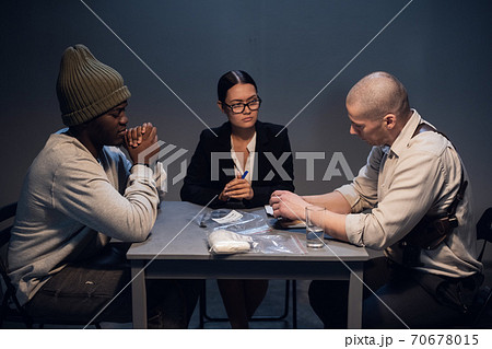 A drug dealer detained with a package containing an unknown white substance is interrogated by an experienced investigator in the presence of a lawyer A drug dealer detained with a package containing an unknown white substance is interrogated by an experienced investigator in the presence of a lawyer 70678015