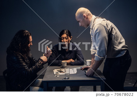 A police investigator with a gun in a holster meets with a man suspected of theft in the presence of a lawyer at the police station 70678022
