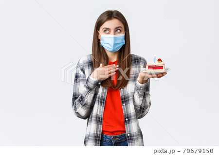 Coronavirus outbreak, lifestyle during social distancing and holidays celebration concept. Dreamy attractive woman in medical mask making wish as holding birthday cake, look away imaging 70679150