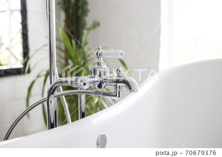 Faucet with shower in the bathroom close-up. Bright white room with greens. Faucet with shower in the bathroom close-up. Bright white room with greens. 70679376