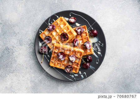 Belgian fluted waffles with fresh cherries and cream on a plate. Soft homemade waffles, sweet dessert with cherries. copy space Belgian fluted waffles with fresh cherries and cream on a plate. Soft homemade waffles, sweet dessert with cherries. copy space 70680767
