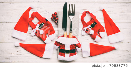 Festive set of fork and knife on wooden background. Top view Banner of new year decorations and santa clothes and hat. Christmas concept with copy space 70683776