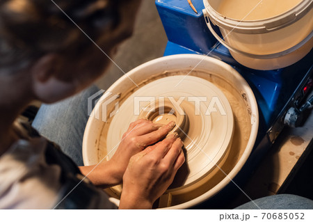 master class on sculpting a pot in an art workshop. the girl behind the potter's wheel makes a blank with her hands. master class on sculpting a pot in an art workshop. the girl behind the potter's wheel makes a blank with her hands. 70685052
