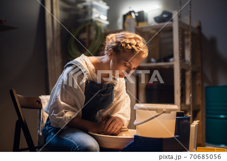 a young blonde potter girl starts making a vase in her workshop on the potter's wheel. 70685056