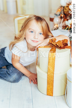Little girl with gift box near Christmas tree on Christmas eve at home. Young kid in light room with winter decoration. Happy family at home. Christmas New Year december time for celebration concept Little girl with gift box near Christmas tree on Christmas eve at home. Young kid in light room with winter decoration. Happy family at home. Christmas New Year december time for celebration concept 70687209