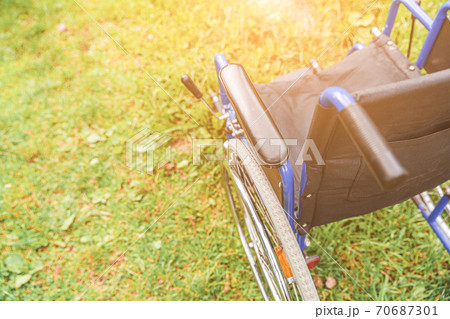 Empty wheelchair standing on grass in hospital park waiting for patient services. Invalid chair for disabled people parked outdoor in nature. Handicap accessible symbol. Health care medical concept. Empty wheelchair standing on grass in hospital park waiting for patient services. Invalid chair for disabled people parked outdoor in nature. Handicap accessible symbol. Health care medical concept. 70687301