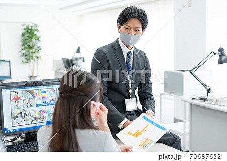 コロナ禍　web会議をしながら上司に指示を仰ぐマスクをつけた会社員 70687652
