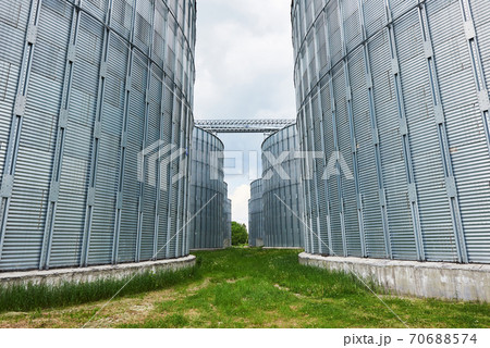 Agricultural Silos. Building Exterior. Storage and drying of grains, wheat, corn, soy, sunflower against the blue sky with white clouds Agricultural Silos. Building Exterior. Storage and drying of grains, wheat, corn, soy, sunflower against the blue sky with white clouds 70688574