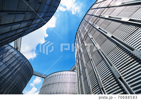 Agricultural Silos. Building Exterior. Storage and drying of grains, wheat, corn, soy, sunflower against the blue sky with white clouds 70688583