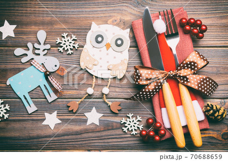 Top view of fork and knife on napkin on wooden background. Different christmas decorations and toys. Close up of New Year dinner concept Top view of fork and knife on napkin on wooden background. Different christmas decorations and toys. Close up of New Year dinner concept 70688659