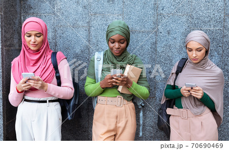 Three Modern Muslim Women Using Cellphones Standing Over Gray Wall Three Modern Muslim Women Using Cellphones Standing Over Gray Wall 70690469