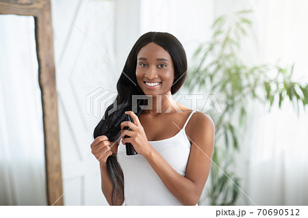 Happy african american millennial woman applying hair oil to prevent split ends 70690512