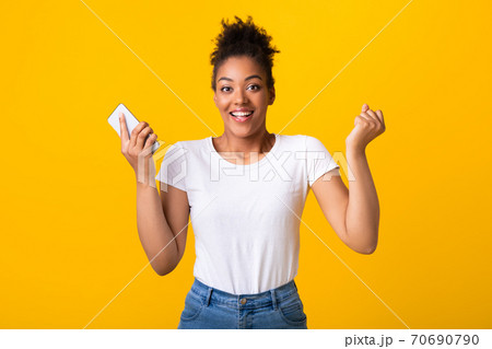 Excited afro lady feeling ecstatic holding smartphone Excited afro lady feeling ecstatic holding smartphone 70690790
