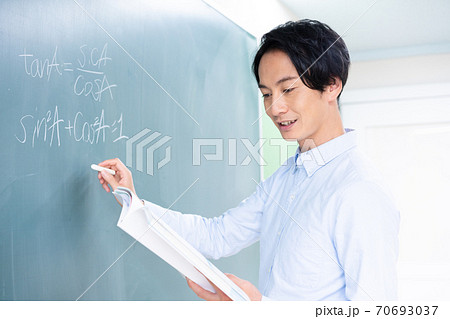 黒板に数式を書く笑顔の若い男性教師の写真素材