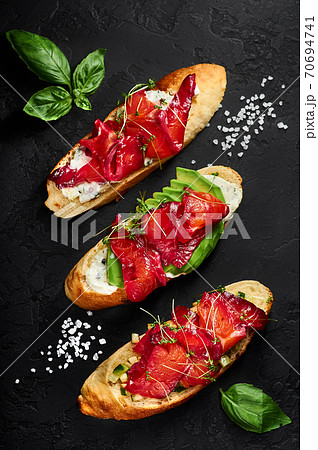 Three salmon bruschettas with avocado and greens on black backdrop decorated with sea salt and basil 70694741