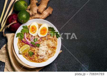 Mohinga or Burmese Fish Noodle Soup in white plate on dark table top. Mohinga or Burmese Fish Noodle Soup in white plate on dark table top. 70694769