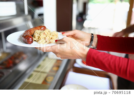 Female hands hold plate with lunch on it sausage and stewed cabbage in bistro 70695118