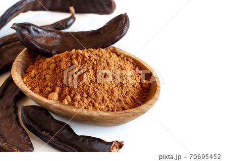 Dry carob powder and pods in a wooden bowl close up Dry carob powder and pods in a wooden bowl close up 70695452
