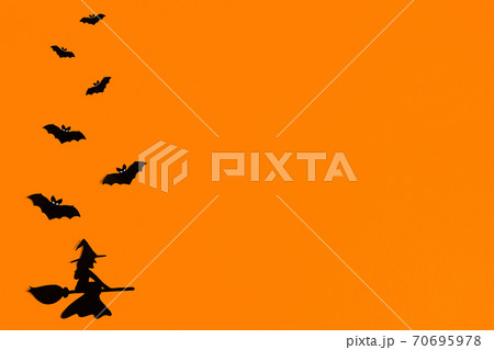 Silhouettes of a flock of bats and a witch flying on a broom made of black paper on an orange 70695978